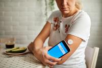 woman holding her phone next to a glucose sensor taped to her arm